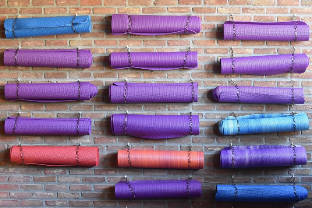 Viele farbige Yogamatten sind an kleinen Ketten an einer Ziegelwand aufgehangen.